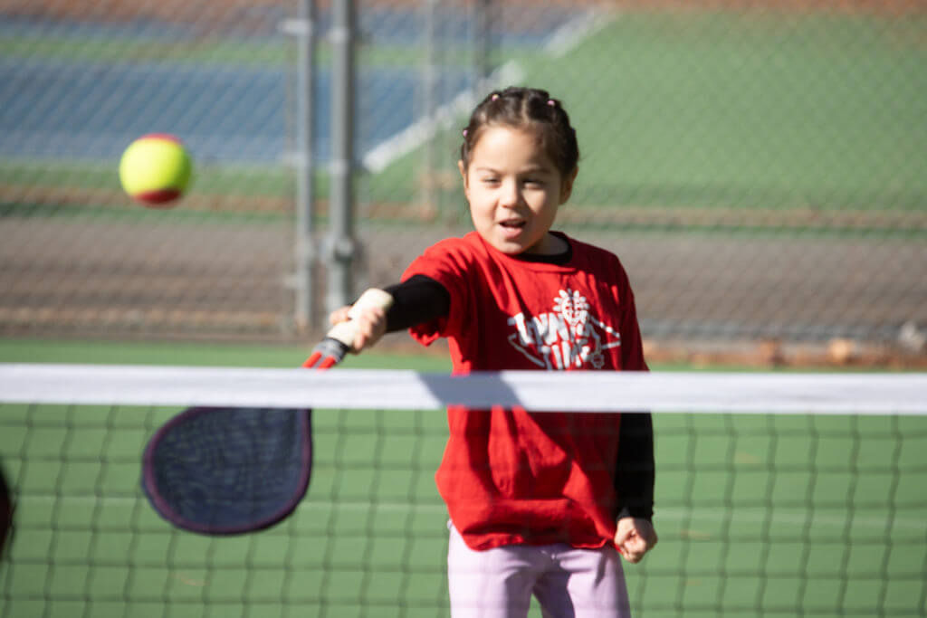 Child playing tennis outdoors to stay active and healthy instead of watching screens.