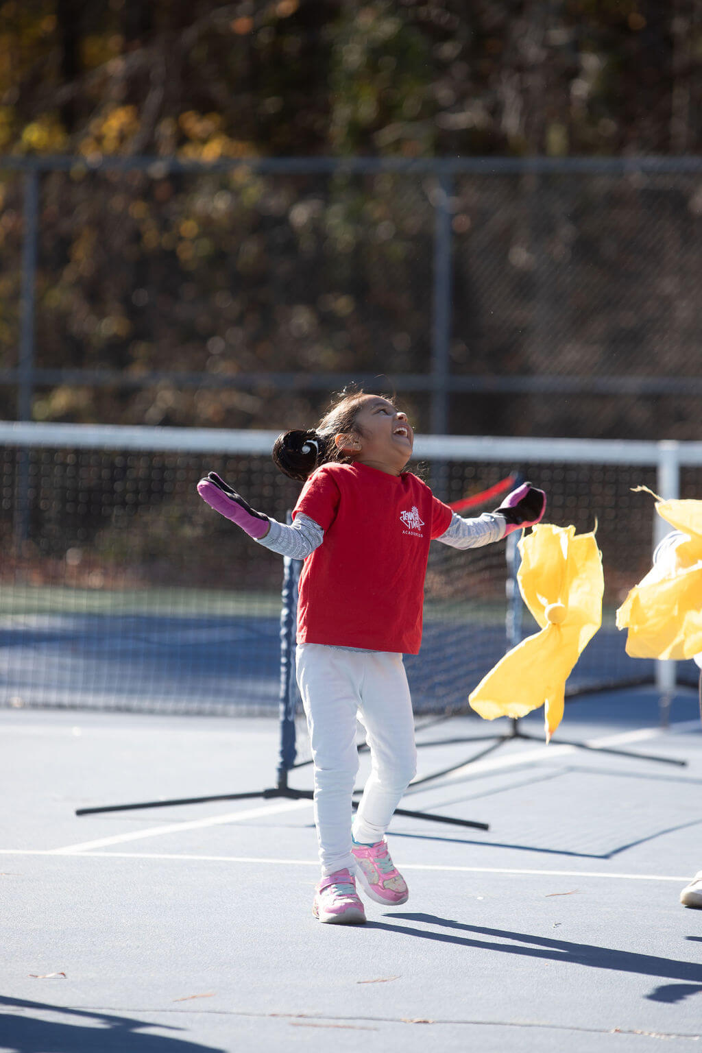 Young girl smiling mid-drill on the tennis court, celebrating a moment of joy during beginner tennis lessons for kids.