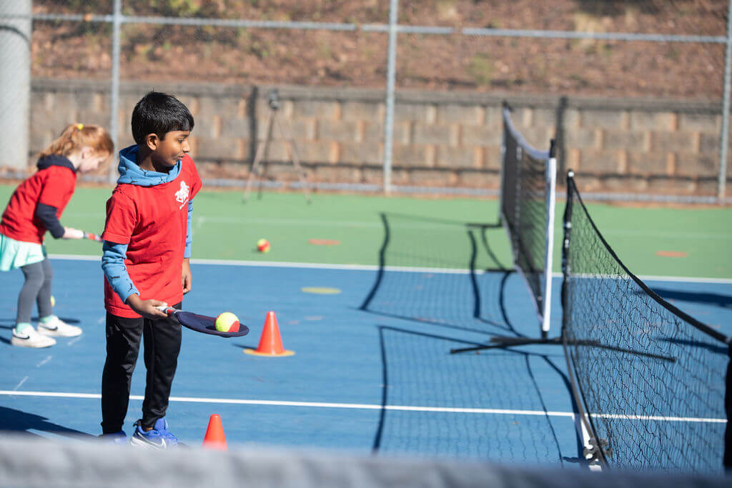 Young child learning tennis with a coach using a soft SMART Racket™ at Tennis Time Academies