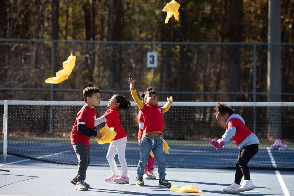 A group of smiling 4-year-olds playing a flying fox on the court.