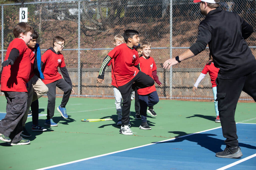 Child practicing tennis footwork drills outdoors with a coach guiding nearby