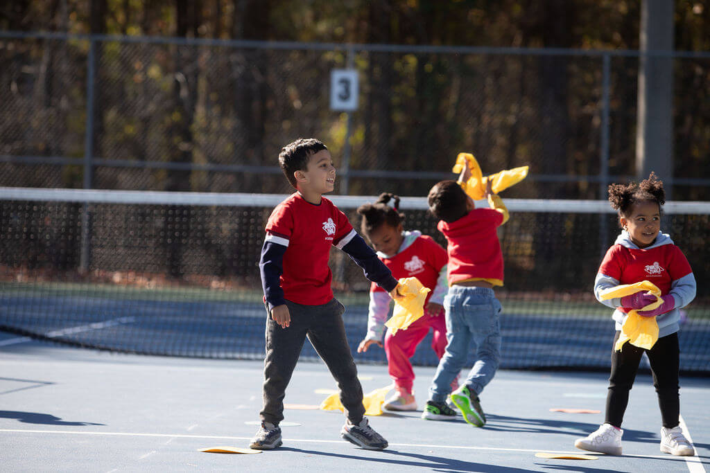 Kids playing a fun movement game on a tennis court during a Tennis Time class.
