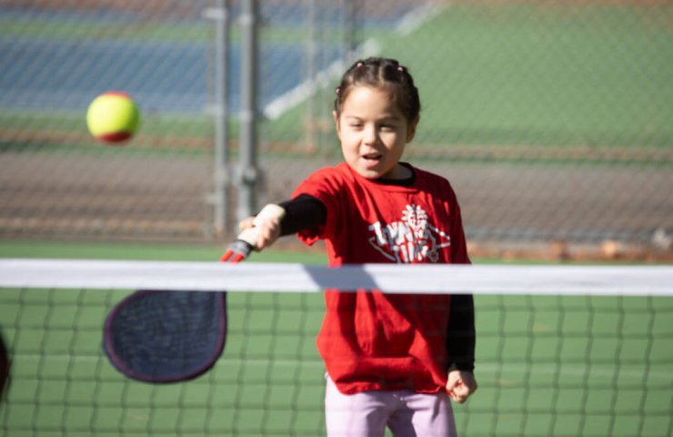Child playing tennis outdoors to stay active and healthy instead of watching screens.
