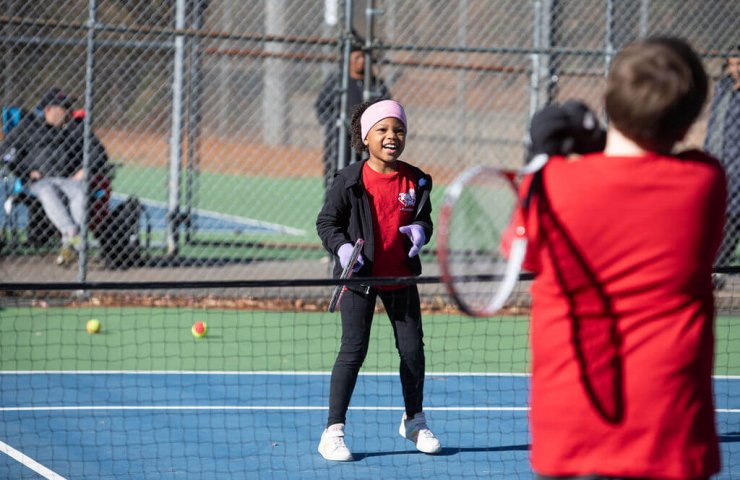 Young children smiling and playing a tennis group game together during a class
