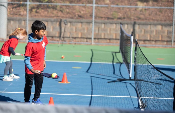 Young child learning tennis with a coach using a soft SMART Racket™ at Tennis Time Academies