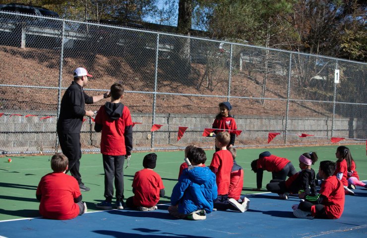 A group of young students attentively listening to their tennis coach during a SMART Tennis™ class, showing focus and engagement.