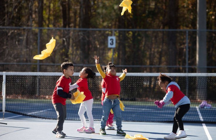 A group of smiling 4-year-olds playing a flying fox on the court.